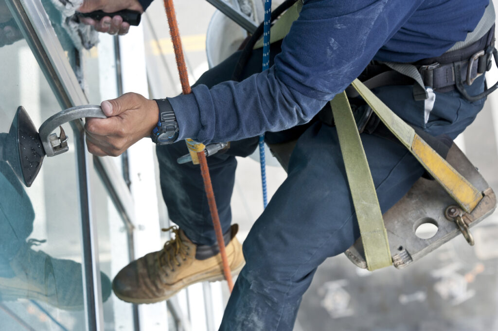 A window washer sitting on a Bosun's chair cleaning high-rise windows